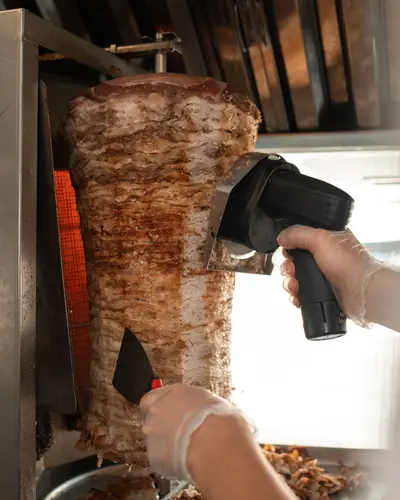 Un cuisinier tranche la viande d'une broche de döner